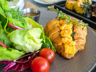 Warm cooked croissant with spinach inside topping with cream cheese, served with vegetable salad in restaurant