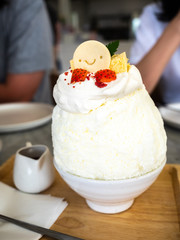 Kakigori, Japanese shaved ice dessert flavored with condensed milk, topping with smiled cookey, strawberry and whipping cream on table in restaurant