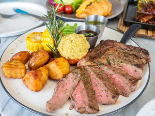 Ribeye beef steak medium to well done grilled served with corn, pototoes and asparagus in restaurant