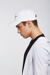 Cropped side photo of a dark-haired man, wearing white baseball cap with lettering 