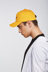 Cropped side photo of a dark-haired man, wearing yellow baseball cap with lettering 