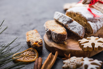 Stollen. sliced homemade Christmas dessert stollen with dried berries and nuts on stone  rustic table with cinnamon, orange slices, Christmas tree branches, gingerbread , selective focus