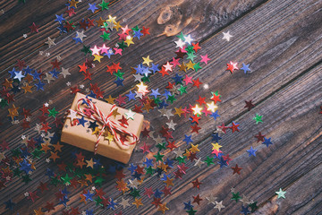Gift box with star. Creative concept with festive decor on black background. Confetti stars, red, yellow with gift box. Explosion of confetti. Toned