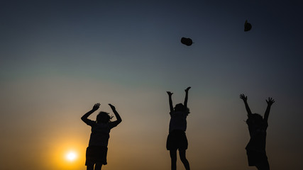  three children silhouetted against a sunset, they are jumping up to catch something in the air.