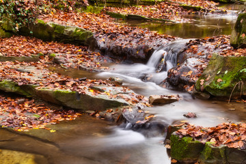 Fototapeta na wymiar Long exposure photo of the tiny creek and waterfall in the forest of Óbánya, Hungary in autumn