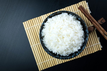 Cooked jasmine rice in ceramic cups and chopsticks Placed on a black wooden table. Close up shot. Top view.