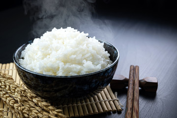 Cooked jasmine rice in ceramic cups and chopsticks and Ear of rice Placed on a black wooden table....