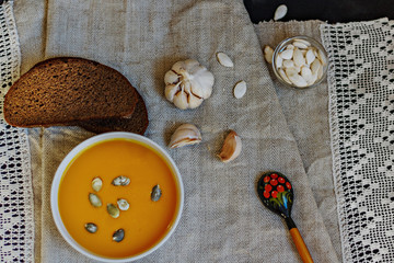 Composition on a homemade linen linen made of pumpkin puree soup, garlic, black bread, pumpkin seeds. Still life.