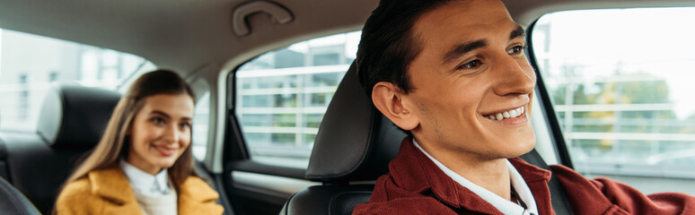 Selective focus of smiling taxi driver and woman on back seat of car, panoramic shot