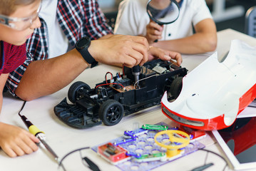 Group of young male pupils with Asian scientist repair radio-controlled car model.