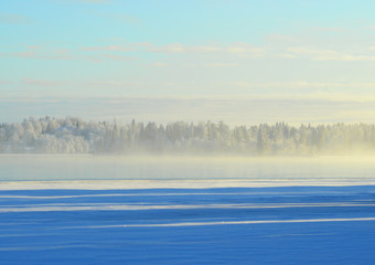 Finnish winter. Crystal clear cold winter day. Lake Porontima, Kuusamo. Bright colors and snowy forest on backround.Mist on the lake and pastel color cloudletts.