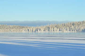 Finnish winter. Crystal clear cold winter day. Lake Porontima, Kuusamo. Bright colors and snowy forest on backround. Beautiful frozen lake landscape.