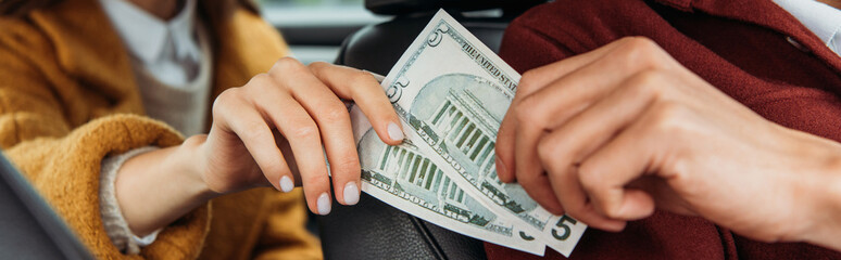 Cropped view of passenger giving dollar banknotes to taxi driver, panoramic shot