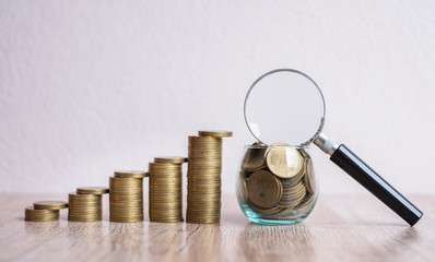 A magnifying glass on a coin in a glass jar. Coin ladder from low to high. Business concepts, investments and risks.The concept of finding investment sources and fund sponsors Find available loans.