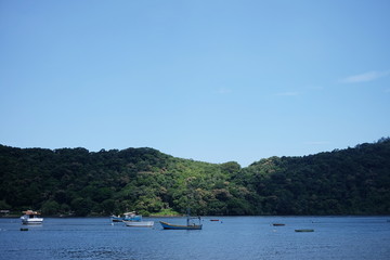 A fisshing boats are standing on the small river close to Bertioga Brazil on a sunny day before the hills with green woods, wild nature life