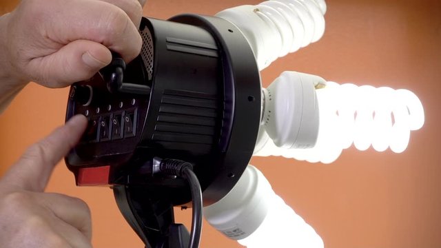 Close POV slow motion shot of a man&rsquo;s hands holding a professional video light and flicking five switches in turm to activate the daylight balanced spiral bulbs.