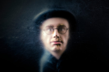 Mystery figure with hat and glasses behind a dusty scratched glass.