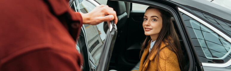 Over shoulder view of taxi driver opening car door for woman, panoramic shot