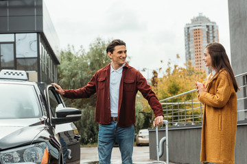 Smiling taxi driver helping young woman with luggage beside car