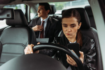 Thoughtful taxi driver using smartphone with businessman at background