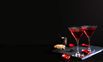 Two cosmopolitan cocktails in a triangular glass. Dark luxury background. In the background an old silver bowl, a bag of tobacco and scattered rose petals.There is also ample copy space.