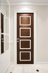 The door is made of walnut wood in a classic style with white architraves in the hallway