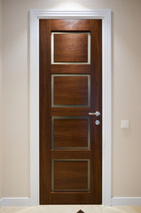 The door is made of walnut wood in a classic style with white architraves in the hallway