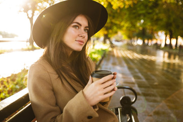 Portrait of thoughtful woman sitting on bench with coffee cup in autumn park