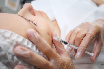 Obraz na płótnie Canvas doctor-cosmetician adds missing volume to cheekbones injecting gel-like medicine under skin selective focus