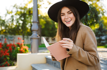 Portrait of beautiful woman wearing coat and hat reading book outdoors