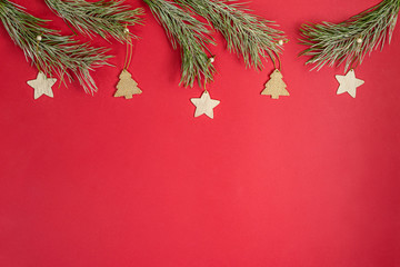 A Christmas toy wooden homemade in the form of a stars hanging on a pine branchs with hoarfrost. Flat lay top layout on red background with copy space.