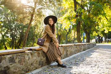Image of brunette woman sitting on bench while walking in green park outdoors