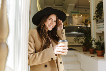 Image of joyful young woman holding coffee cup at indoor cafe