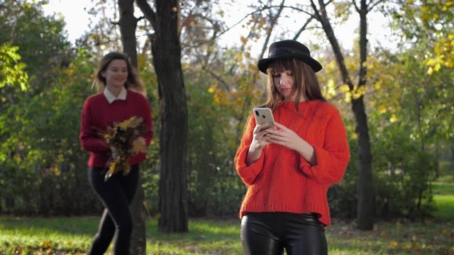 cheerful female friends take pictures for memory during a joint holiday in the autumn park on a warm day in the fall season