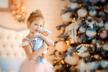 5 years old girl in beautiful light pink dress with doll in blue clothes in christmas time