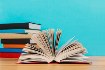 A simple composition of many hardback books, raw books on a wooden table and a bright blue background
