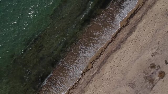 Overhead aerial drone shot  over a golden sandy shore and the blue sea of Mediterranean sea close to Thessaloniki, Greece in Epanomi