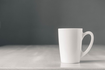 White ceramic cup on white wooden table on gray background. Place for text or advertising