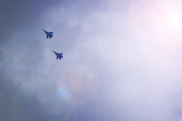 Two military fighters fly in the sky. Behind them stretches a condensation trail.