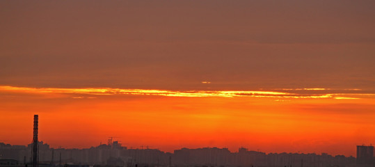 Naklejka premium The colorful dramatic sunset sky in an industrial zone of a city.Silhouettes of house and chimneys.