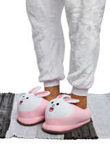 Close-up shot of male legs in white velour trousers and white and pink plush house slippers made in...