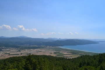 The sea captured from the seaside, there are hills and blue sky. Captured in daytime.