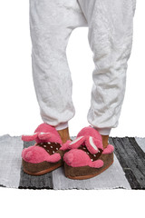 Close-up shot of male legs in white velour trousers and brown plush house slippers with a pink rabbit in polka-dot shirt. The man is standing on the striped gray and white carpet.