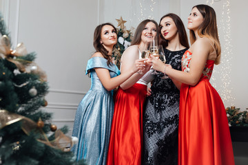 Gorgeous girls In stylish sexy party dresses holding glasses with champagne. Christmas fun. Smiling young girls with professional make up and hairstyle. New year concept. 