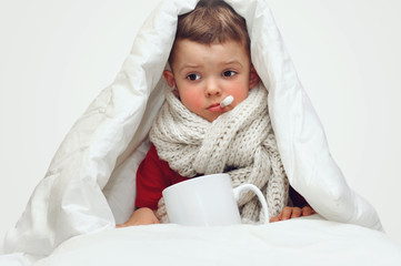 A little cute boy gets sick and measures the temperature with an oral thermometer and sits covered...