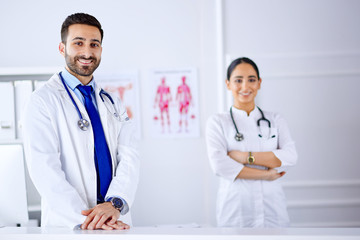 Two young smiling arab doctors standing in consultation room in hospital