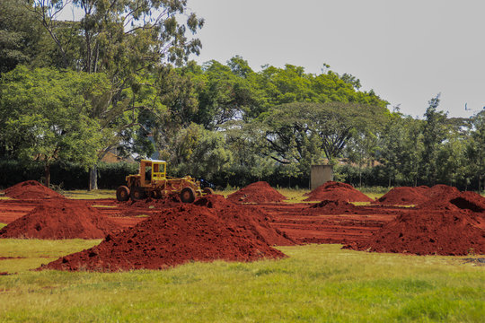 Piles of bright, saturated and oily red soil on a field with a tractor in Nairobi, Kenya.