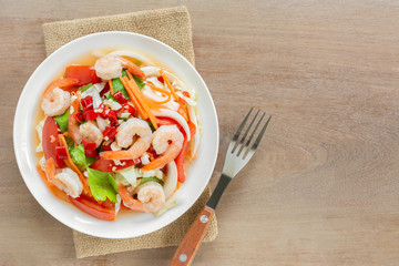 top view of spicy shrimps salad in a ceramic dish on wooden table. delicious thai style food menu.