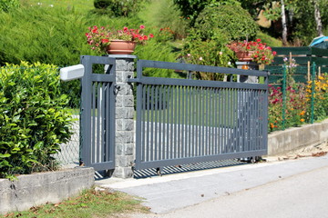 Thick strong metal sliding front yard driveway entrance doors mounted on stone column surrounded...