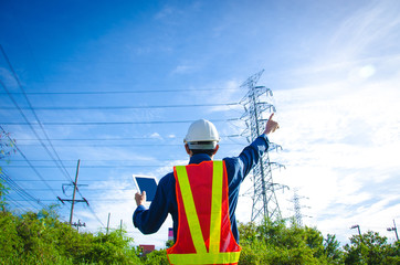 Engineer pointing at high voltage power pylon against blue sky background.